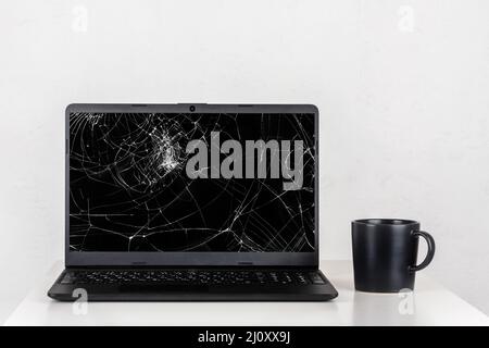 https://l450v.alamy.com/450v/2j0xx9j/a-laptop-with-a-broken-screen-and-a-black-mug-of-tea-on-a-table-against-a-white-wall-2j0xx9j.jpg