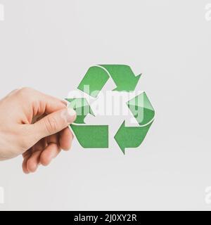 Person s hand holding green recycle symbol white backdrop. High quality photo Stock Photo