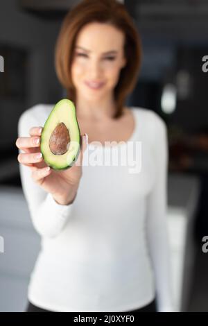 Young Caucasian woman holding halved avocado depth of field, vertical Stock Photo