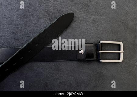 Fashionable men's black belt made of genuine leather with a light metal buckle on a dark background. Stock Photo