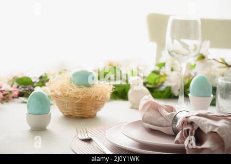 Easter table setting with blue eggs, spring decorations, fresh flowers. Elegance dinner in interior. Close up. Stock Photo