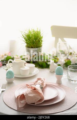 Easter table setting with blue eggs, festive decorations, fresh flowers. Elegance dinner at home interior. Vertical format. Stock Photo