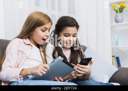 Happy female friends sitting sofa using digital tablet mobile phone. High quality photo Stock Photo