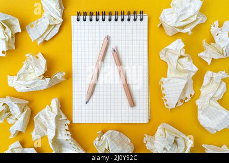 Red pencil and notebook on a yellow background. Crumpled sheets of paper. Stock Photo