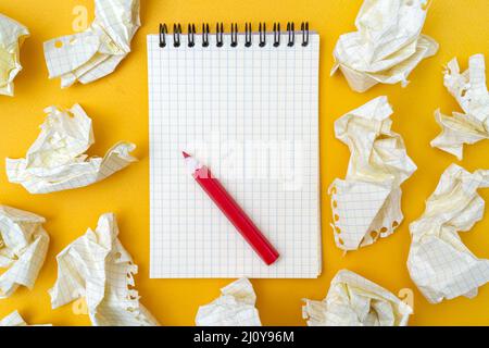 Red pencil and notebook on a yellow background. Crumpled sheets of paper. Stock Photo