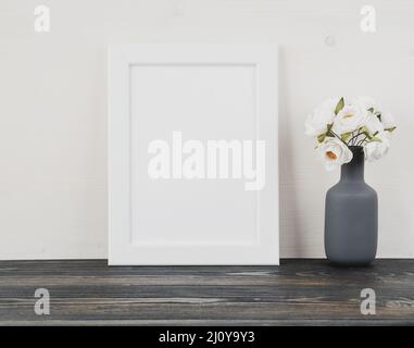 White frame, flower in vase, clock on dark grey wooden table against white wall with copy space Stock Photo