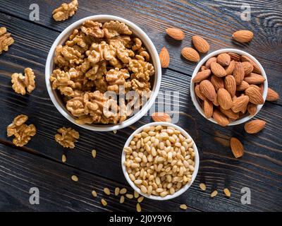 Assorted nuts in white bowl on wooden dark background, mix of walnuts, almonds and cedar, top view Stock Photo