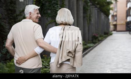 Back view embraced older couple taking walk outdoors. High quality photo