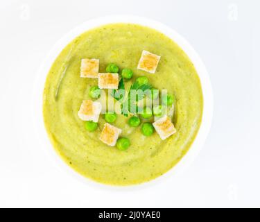 Large white bowl with cream soup of broccoli, potatoes and green peas on white background, top view Stock Photo