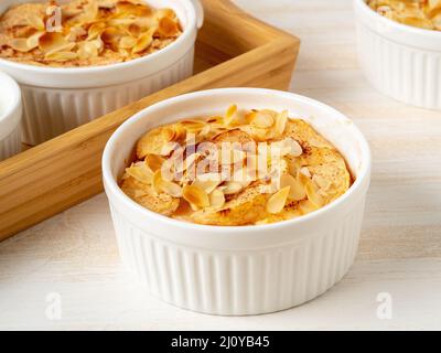 Cheesecake on white wooden table in kitchen. Delicate curd dessert with apples, almond flakes Stock Photo