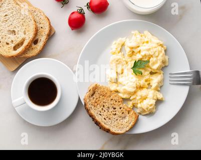 Breakfast with pan-fried scrambled eggs, cup of coffee, tomatoes on white stone background. Stock Photo