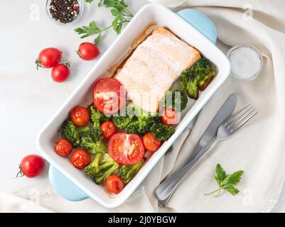 Fish salmon baked in oven with vegetables - broccoli, tomatoes. Healthy diet food, white marble backdrop, top view. Stock Photo