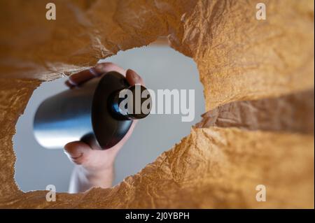A hand places a black plastic bottle from a paper bag. A mature man's hand holds a bottle of shampoo or shower gel over the open brown bag. Shot from Stock Photo