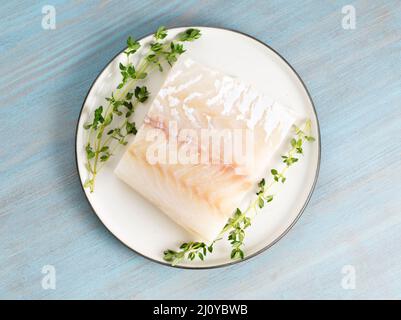 Piece of raw cod fish fillet on plate on blue wooden table, top view Stock Photo