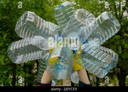 Garbage collection. Hands in yellow gloves holding big empty plastic bottles. Grass on a background. Stock Photo