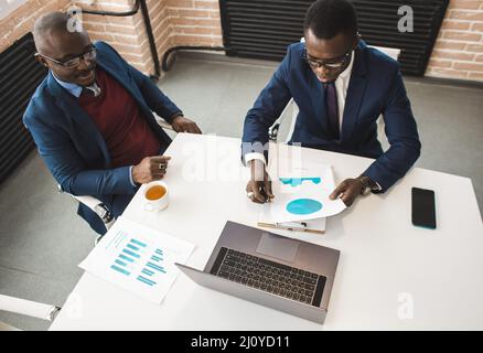 Two African American business partners are working on a laptop studying stock market charts and technical analysis. Training in investment and Stock Photo