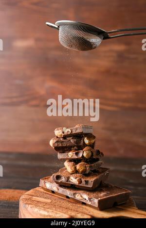 Sprinkling of cacao powder onto pieces of tasty chocolate with nuts on wooden background Stock Photo