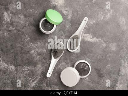 Jars of activated carbon facial mask and spoons with powder on grunge background Stock Photo