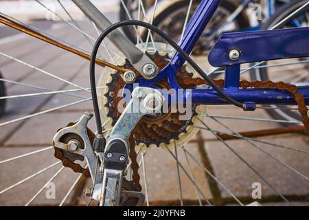 Blue bike has been outside all winter and got broken. Rusty bicycle chain hangs on sprocket and gear. Stock Photo