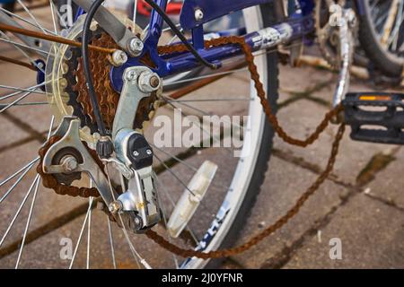 Blue bike has been outside all winter and got broken. Rusty bicycle chain hangs on sprocket and gear. Stock Photo