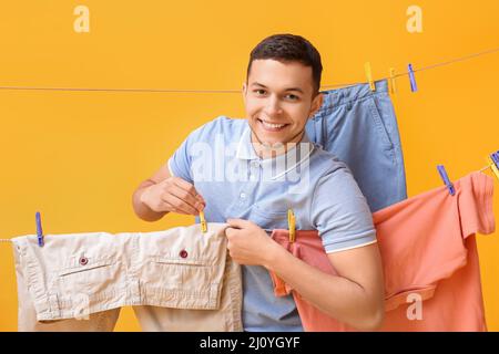 Young man hanging clean shorts with plastic clothespin on yellow background Stock Photo