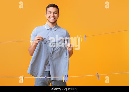 Young man hanging clean shorts with plastic clothespin on yellow background Stock Photo