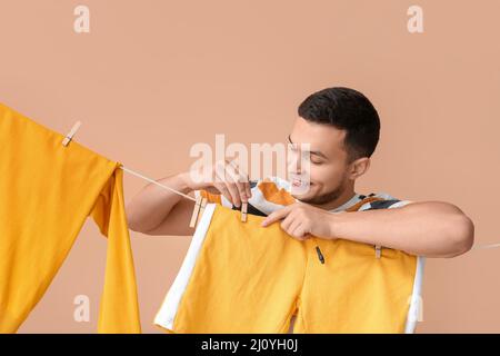 Young man hanging clean shorts with wooden clothespin on beige background Stock Photo