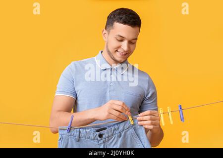 Young man hanging clean shorts with plastic clothespin on yellow background Stock Photo