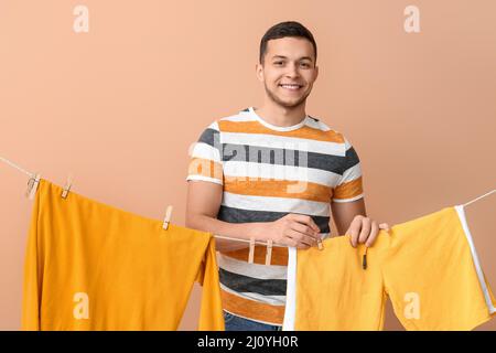 Young man hanging clean shorts with wooden clothespin on beige background Stock Photo