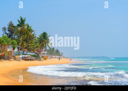Hikkaduwa, Sri Lanka. March 6, 2018. Sunny Beach on Indian Ocean. Palm trees on sandy shore. People on coast. Stock Photo