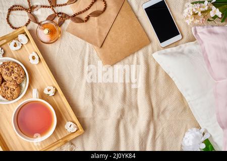Mockup with women's accessories on bed tea, cookies, pillows, flowers, letter, notebook. Stock Photo