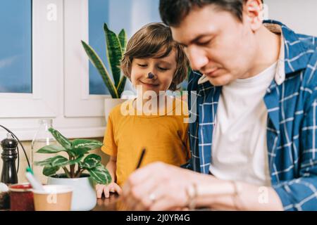 Easter day. Male Father and son painting eggs on wooden background. Family sitting in a kitchen. Preparing for Easter, creative homemade decoration Stock Photo