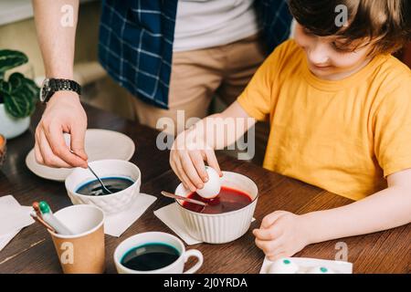 Easter day. Male Father and son painting eggs on wooden background. Family sitting in a kitchen. Preparing for Easter, creative homemade decoration Stock Photo