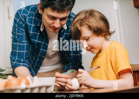 Easter day. Male Father and son painting eggs on wooden background. Family sitting in a kitchen. Preparing for Easter, creative homemade decoration Stock Photo