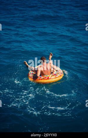 A man floats on an inflatable ring in the sea with blue water. Vacation at the sea on a sunny day. Turkey vacation concept Stock Photo