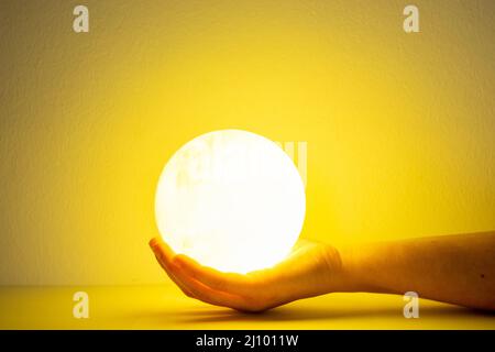 Moon lamp turn on with yellow background hold by one hand Stock Photo
