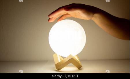 Moon lamp turn on with white background with a hand over it