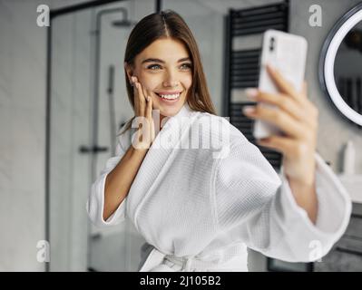 Positive young woman bathrobe taking selfie Stock Photo