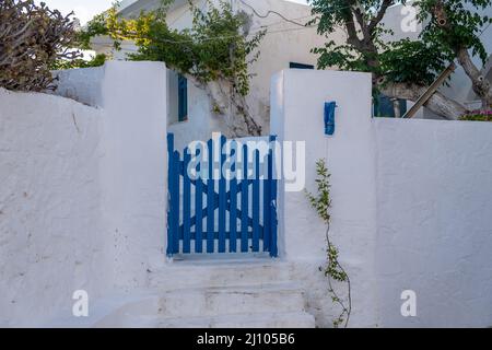 Greek Island, Cyclades. Blue wooden fence entrance gate close,  whitewashed stonewall, plant at yard. Greece Summer holiday destination. Stock Photo