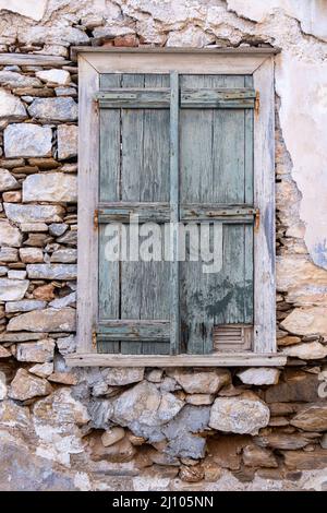 Green wooden shabby window, aged building stonewall background, front view. Abandoned old house, Greek Island, Greece. Stock Photo