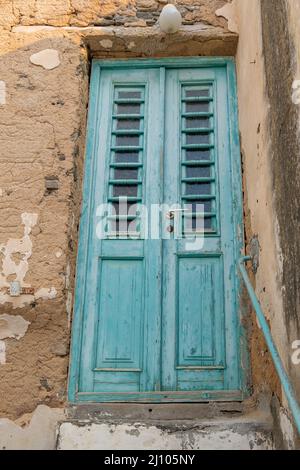 Greek Island, Greece. Abandoned building with peeled wall, blue wooden close aged faded door. Under view. Vertical Stock Photo