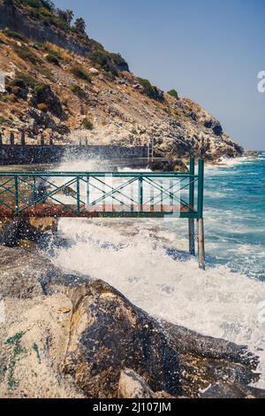 Sea water beats against rocky rocks and makes waves with foam, rugged pier in the sea Stock Photo