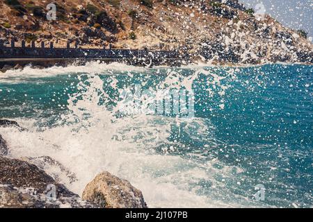 Sea water beats against rocky rocks and makes waves with foam, rugged pier in the sea Stock Photo