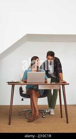Hows it going over here, honey. Shot of a happy young man checking in on his wife while she works from her desk at home. Stock Photo