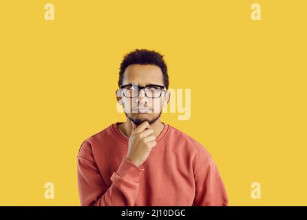 Confused student in glasses doubting something and thinking hard with hand on his chin Stock Photo