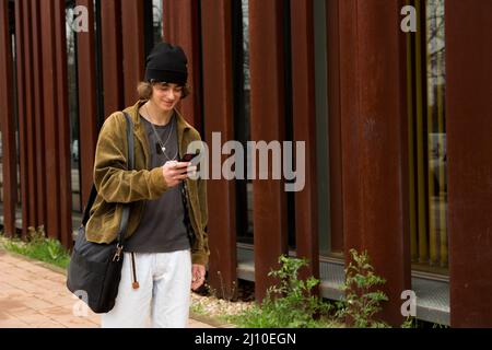 young man in cap walking down the street using mobile phone with briefcase Stock Photo