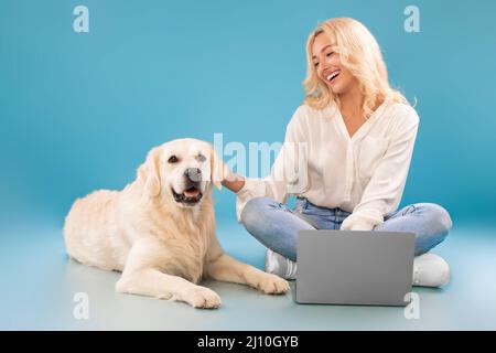 Young woman using pc sitting on floor stroking happy dog Stock Photo
