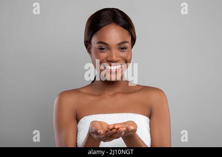 Happy Black Female Wrapped In Bath Towel Demonstrating Something On Empty Palms Stock Photo