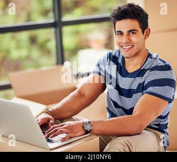 Just moved in and already connected. Portrait of a young man using a laptop while taking a break from moving into a new home. Stock Photo
