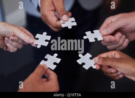 Always welcome help thats offered. Shot of a group of businesspeople putting together puzzle pieces. Stock Photo